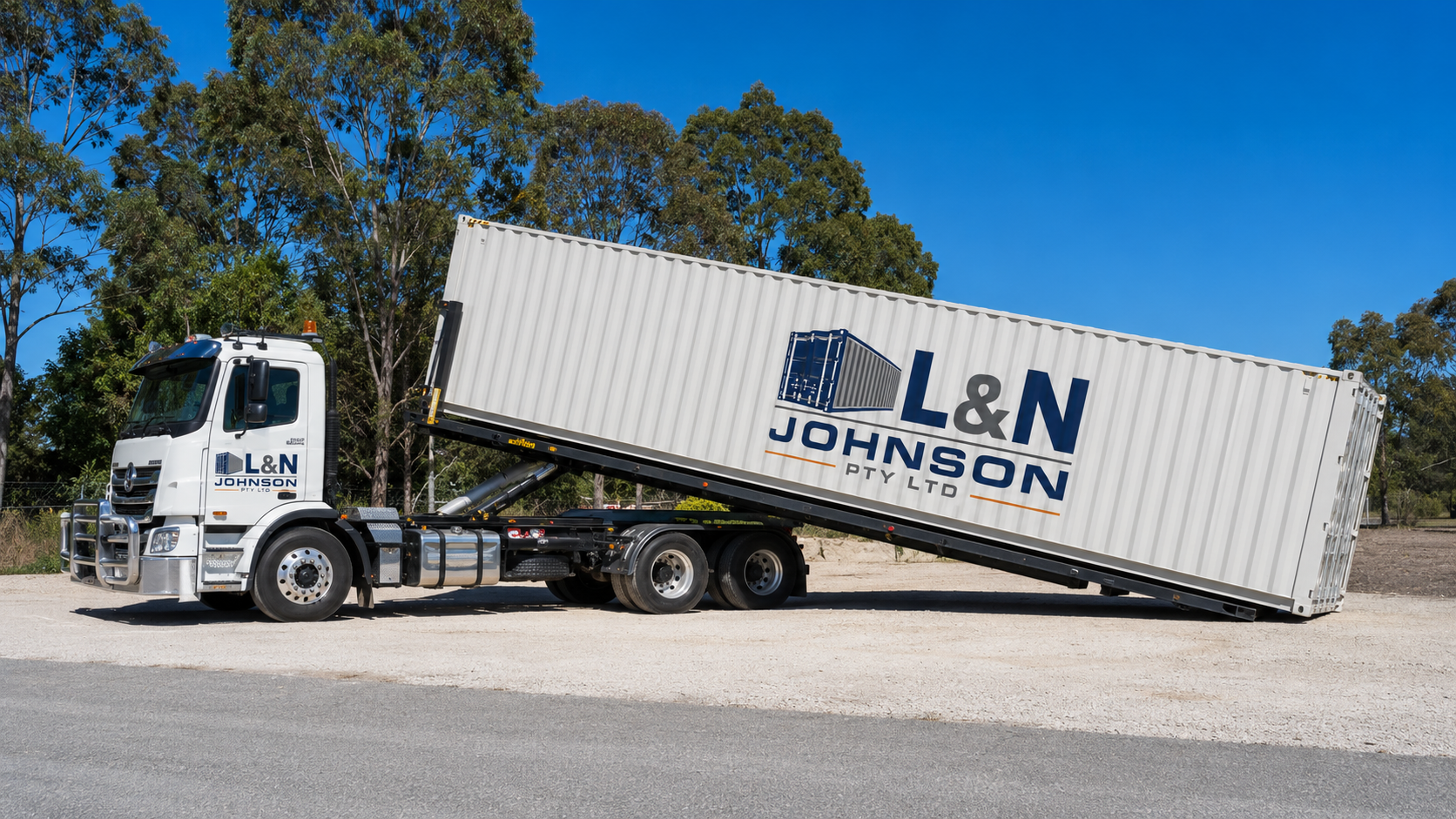 L & N Johnson Pty Ltd tilt tray truck delivering a 40ft shipping container in daylight under a clear blue sky.